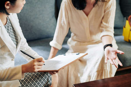 Cosmetologist asking female client questions about her lifestyle and habits and filling questionnaireの写真素材