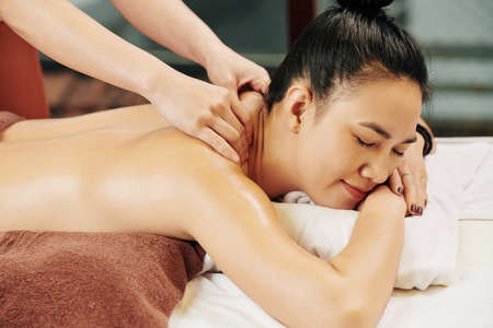 Smiling young Asian woman enjoying shoulder massage with oils in spa salonの写真素材