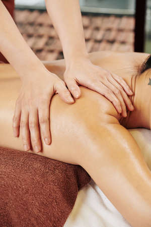 Hands of woman massaging shoulder of female client relazing on bed in spa salonの写真素材