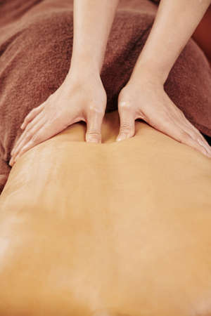 Hands of professional masseur massaging back of young woman with oils in spa salonの写真素材
