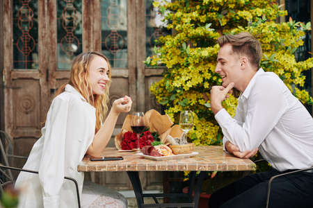 Happy young couple flirting, drinking wine and eating snacks at restaurant tableの写真素材