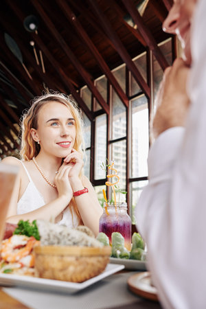 Lovely young smiling woman sitting at cafe table and enjoying dinner with her boyfriendの写真素材