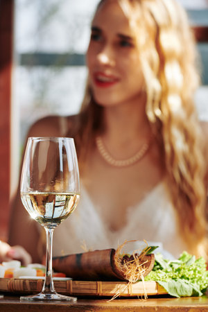 Glass of white wine and appetizer on restaurant table in front of pretty young woman