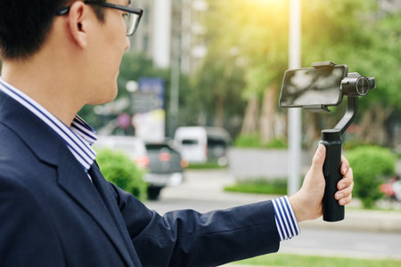 Smartphone attached to monopod in hand of blogger making entertaining video for followers