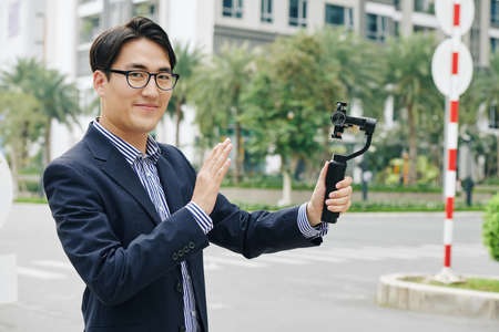 Portrait of Asian man in glasses holding monopod with smartphone and smiling at cameraの写真素材