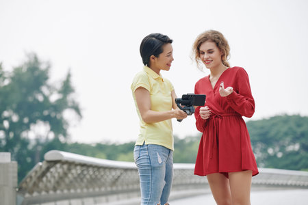 Pretty young smiling woman discussing video on smartphone screen with her camerawomanの写真素材