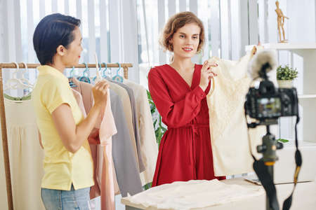 Assistant helping beauty blogger to make fashion haul video for her blog, she is giving her clothes from the rackの写真素材