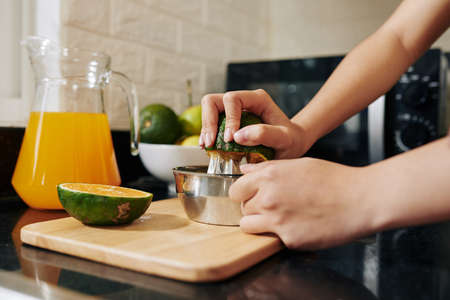 Close-up image of woman using manual metal squeezer when making fresh orange juice for breakfastの写真素材