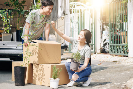 Pretty young Vietnamese woman checking plant leaves after transporting it to new house