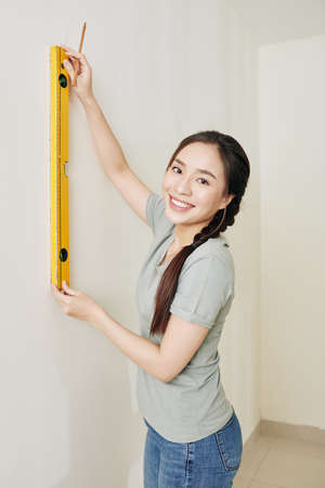 Pretty young Vietnamese woman using spirit livel when marking dot on the wall for hanging pictureの写真素材