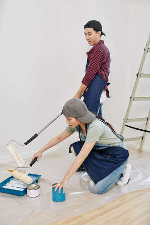 Young Asian couple with foam rollers painting walls in bedroom in white colorの写真素材