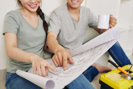 Close-up image of smiling young couple drinking coffee and discussing construction plan of their new houseの写真素材