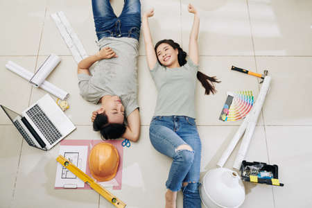 Happy satisfied young Vietnamese couple resting on the floor after planning home renovation, view from aboveの写真素材