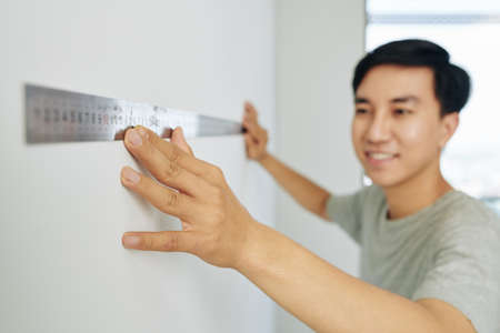 Smiling young man using metal ruller when measuring walls in his apartmentの写真素材