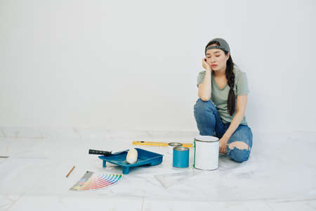 Pretty young woman tired of painting walls in her new apartment, she is resting on the floor with her eyes closedの写真素材