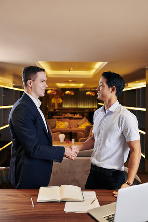Positive multi-ethnic business partners shaking hands before discussing details of work at meeting