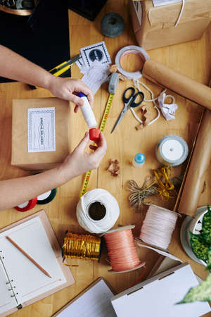 Hands of woman using glue stick when wrapping presents and parcels for friend, family members or customersの写真素材