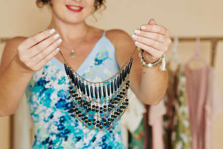 Smiling young woman with manicured hands demonstrating beautiful necklaceの写真素材