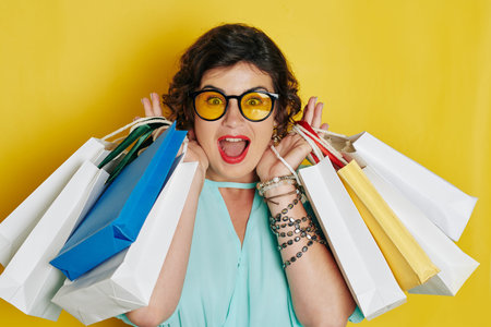 Portrait of excited happy woman in glasses with many shopping bags shouting and looking at camera