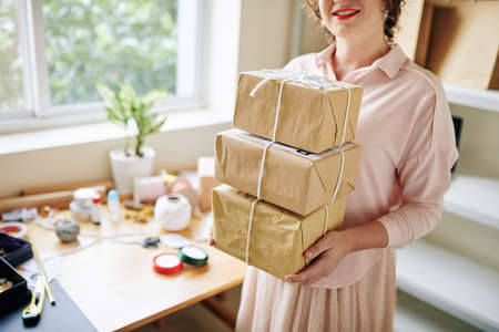 Smiling woman standing in her small home office with stack of parcels ready to be sent to customersの写真素材