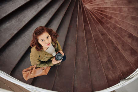 Smiling Vietnamese woman walking down the stairs with cup of coffee and looking up in cameraの写真素材