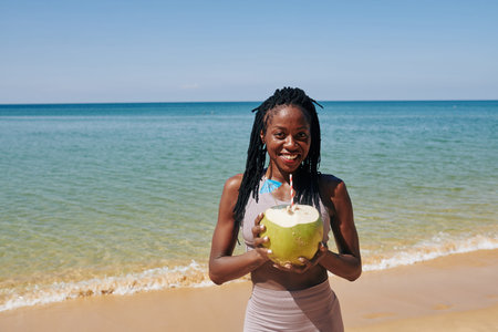 Portrait of beautiful Black young woman with big green coconut and drinking straw