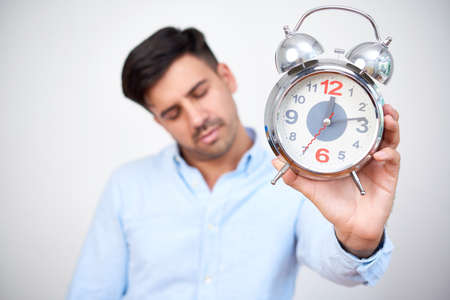 Sleepy tired young entrepreneur showing alarm clock in the morningの写真素材