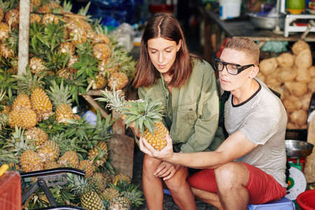 Young Caucasian couple choosing fresh pineapples at local marketの写真素材