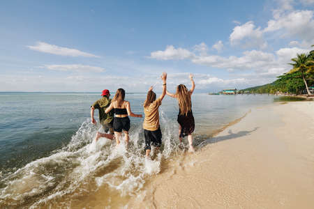 Rear view of happy excited young people running and splashing in water on the beachの写真素材