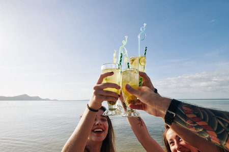 Excited happy young people raising glasses with cold delicious fruit cocktails and celebrating great beach vacationsの写真素材