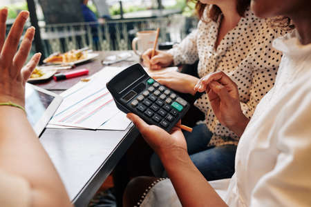 Female friends sitting at cafe table with calculator and plane tickets and discussing travel expensesの写真素材