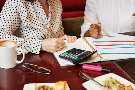 Businesswomen discussing upcoming trip and financial issues after eating lunch in cafe