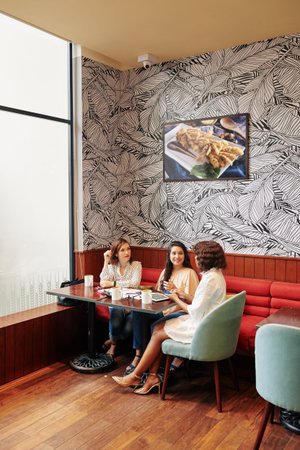 Group of businesswomen sitting at table in small cafe and table about news and ideasの写真素材
