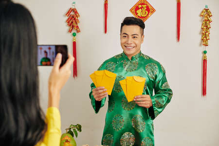 Handsome young Vietnamese man posing in traditional dress with lucky money envelopes at Tet celebrationの写真素材