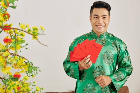 Portrait of young attractive Asian man holding red envelopes for Tet celebrationの写真素材