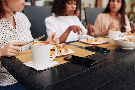 Female coworkers sitting at big table in cafe and eating lunch togetherの写真素材
