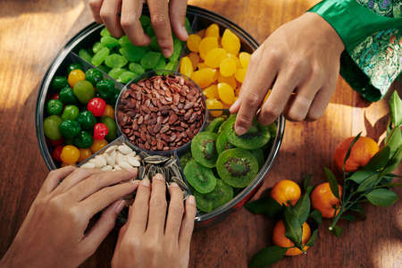 Hands of people taking seeds and dried fruits and berries from good luck food tray served for Lunar New Year celebrationの写真素材