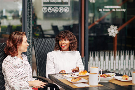 Pretty smiling multi-ethnic friends eating lunch and discussing news and ideas when meeting in cafeの写真素材