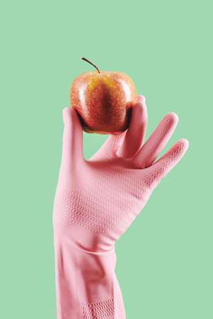 Gloved hand of housewife holding fresh ripe red apple, isolated on greenの写真素材