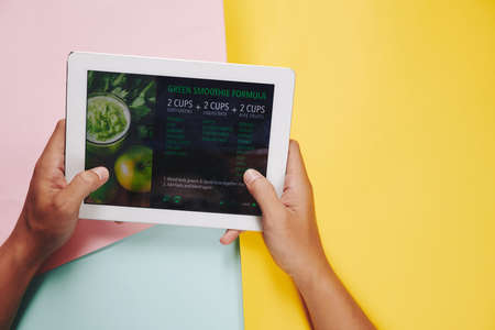 Hands of man holding tablet computer with green smoothie recipe on the screenの写真素材