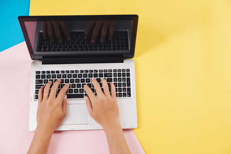 Hands of software developer working on laptop at his colorful desk, view from aboveの写真素材