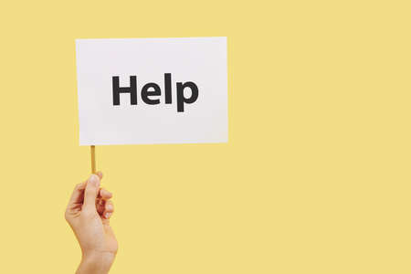 Hand holding small white flag with help inscription, isolated on yellowの写真素材