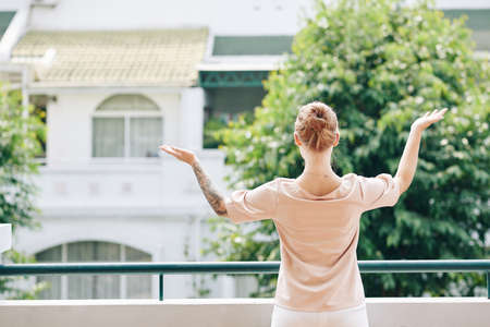 Rear view of young woman standing on balcony and enjoying warm sun raysの写真素材