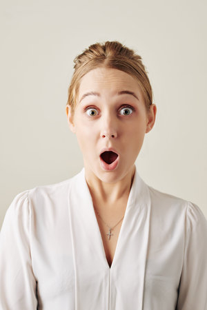 Portrait of shocked excited young businesswoman with wide eyes and mouth opened looking at camera