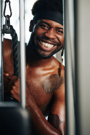 Vertical chest up shot of positive African American man smiling while exercising in gym