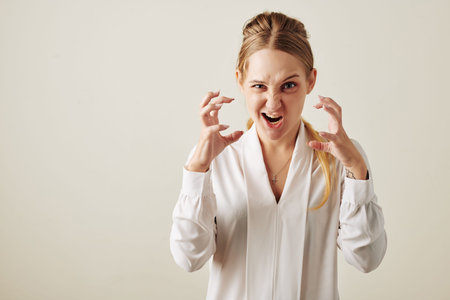 Horizontal waist up studio portrait shot of young Caucasian woman getting ourt of anger roaring