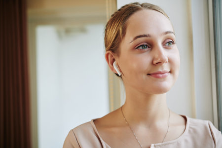 Medium close up portrait shot of charming young woman listening to music in her earphones looking...