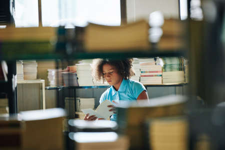 Serious teen student spending time in school library doing homework project horizontal through bookshelf shotの写真素材