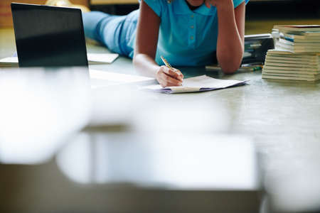 Unrecognizable girl lying on floor doing her homework in school libraryの写真素材
