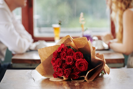 Beautiful bunch of roses lying on cafe table with unrecognizble man and woman having date on backgroundの写真素材